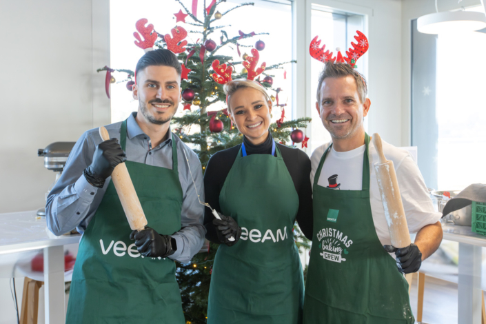 Drei Menschen in grünen Schürzen stehen vor einem Weihnachtsbaum.