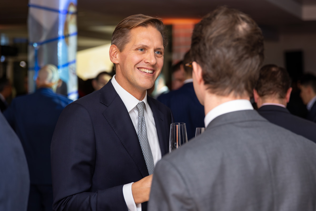 A man in a suit is talking to another man at an event.