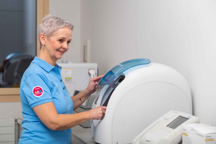 A woman in a blue shirt stands next to a machine.