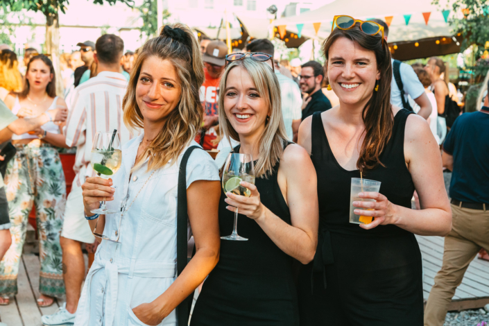 Three women holding drinks at an outdoor party.