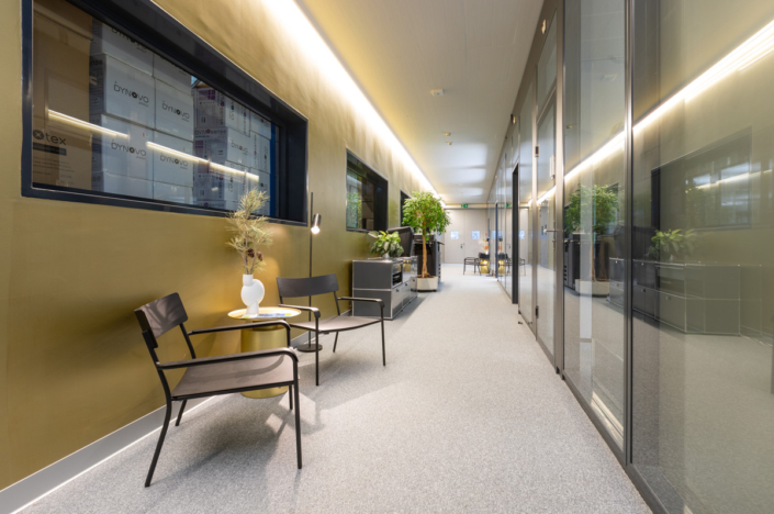 A corridor in an office with a chair and a plant.