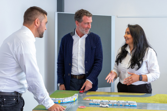 Three people are standing around a table with a model of a train.