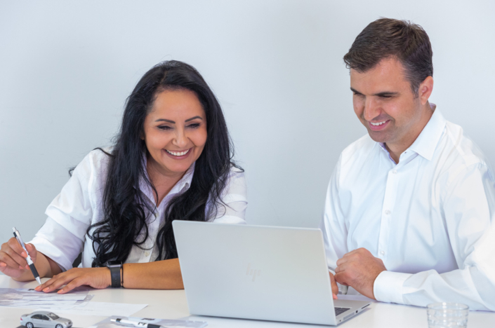 A man and a woman are sitting at a table looking at a laptop.