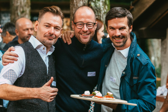 Drei Männer posieren für ein Foto bei einer Outdoor-Veranstaltung.