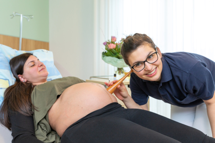 A pregnant woman is helped by a nurse in a hospital.