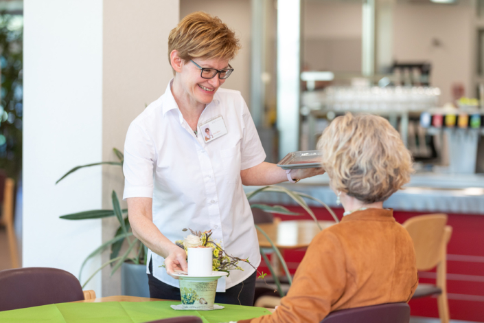 A woman serves a woman in a cafeteria.