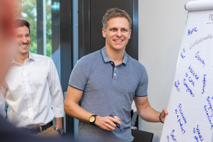 Two men stand in front of an inscribed board.