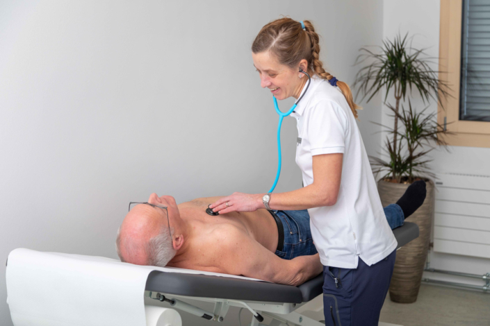 A woman examines an elderly man with a stethoscope.